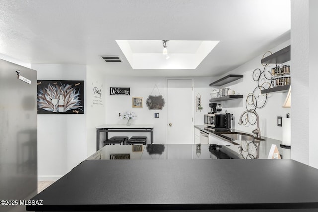 kitchen with dark countertops, visible vents, a sink, a raised ceiling, and open shelves