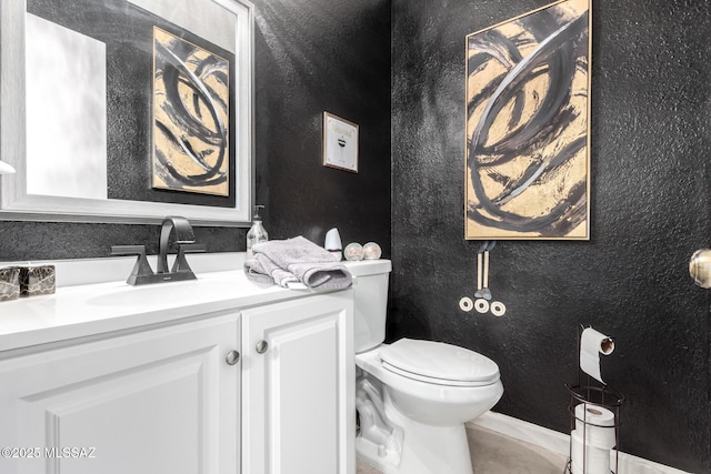 half bath with vanity, toilet, and a textured wall