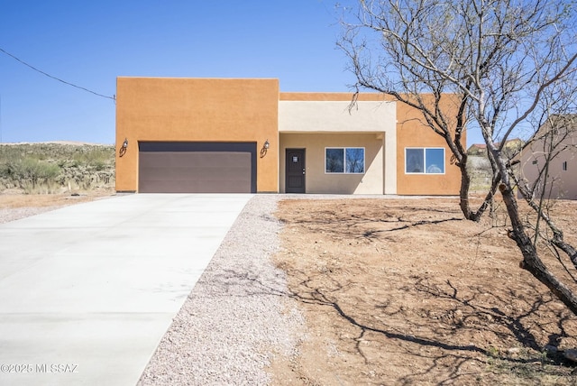 pueblo-style home with driveway, an attached garage, and stucco siding