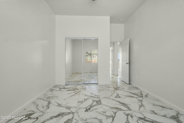 unfurnished bedroom featuring marble finish floor, baseboards, and a closet