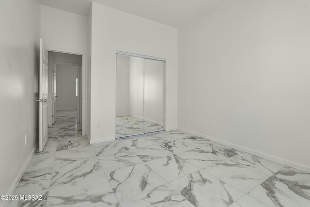 unfurnished bedroom featuring marble finish floor, baseboards, and a closet