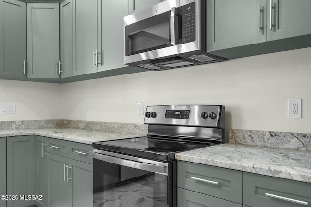 kitchen with stainless steel appliances, light stone counters, and gray cabinets