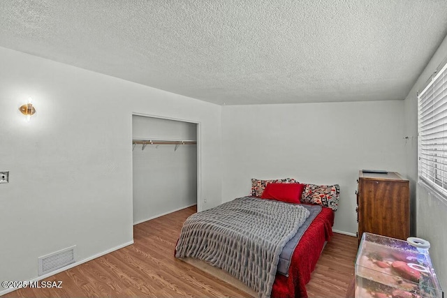 bedroom featuring a closet, a textured ceiling, visible vents, baseboards, and wood finished floors
