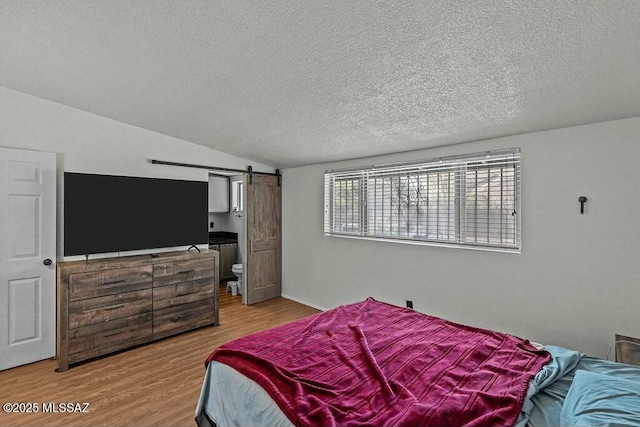 bedroom with a textured ceiling, a barn door, vaulted ceiling, and light wood-type flooring