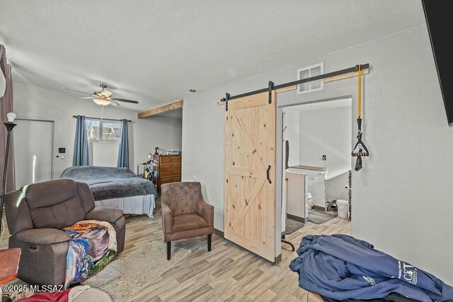 bedroom featuring a ceiling fan, visible vents, a barn door, and light wood-type flooring