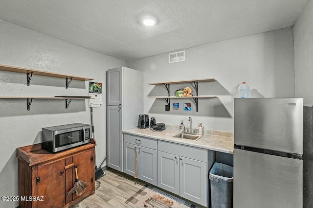 kitchen featuring visible vents, appliances with stainless steel finishes, a sink, open shelves, and gray cabinetry
