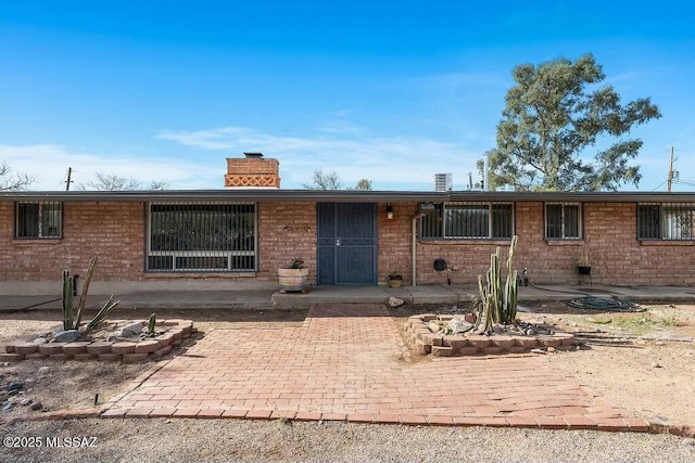 ranch-style house featuring a chimney and brick siding