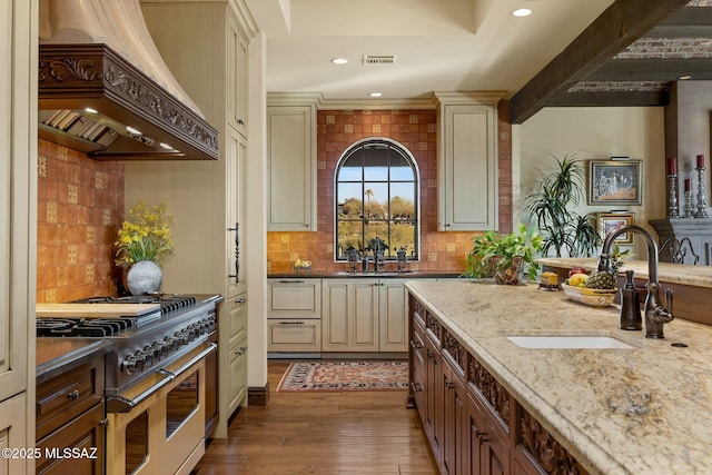 kitchen with range with two ovens, cream cabinets, a sink, visible vents, and custom range hood