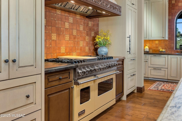 kitchen featuring tasteful backsplash, dark countertops, wood finished floors, double oven range, and premium range hood