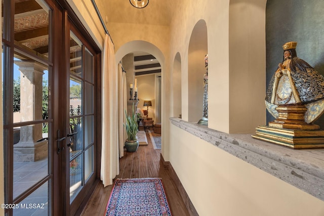 corridor featuring a towering ceiling, dark wood-style floors, baseboards, and arched walkways