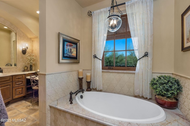 full bathroom with vanity, tile walls, wainscoting, a bath, and an inviting chandelier