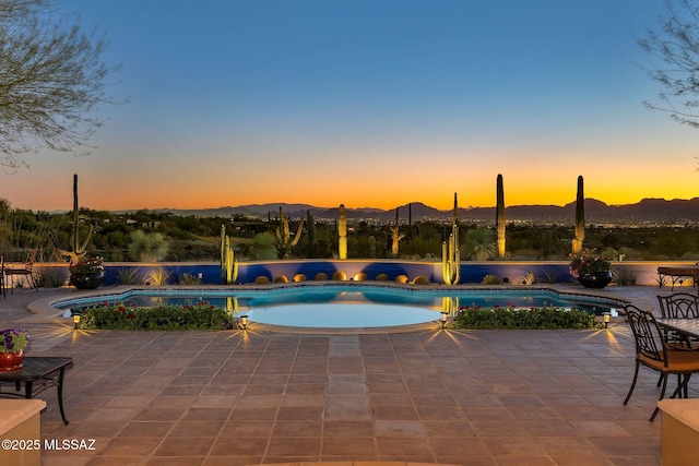 pool at dusk featuring an outdoor pool, a patio area, and a mountain view