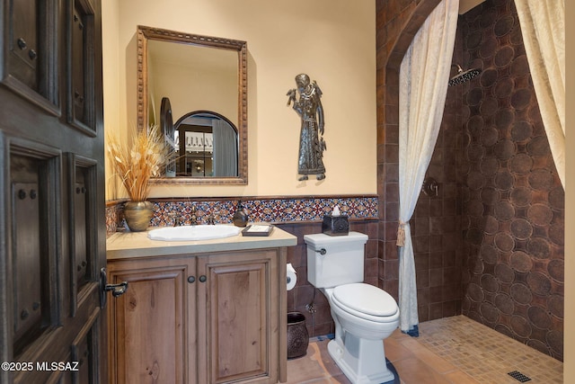 full bath featuring tile walls, toilet, wainscoting, a tile shower, and vanity