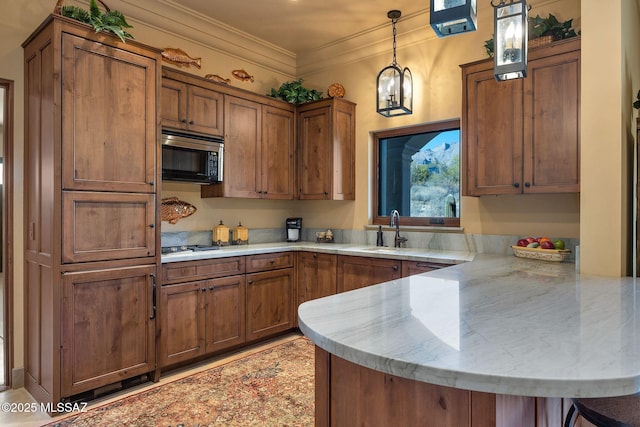 kitchen with a peninsula, a sink, brown cabinets, stainless steel microwave, and decorative light fixtures