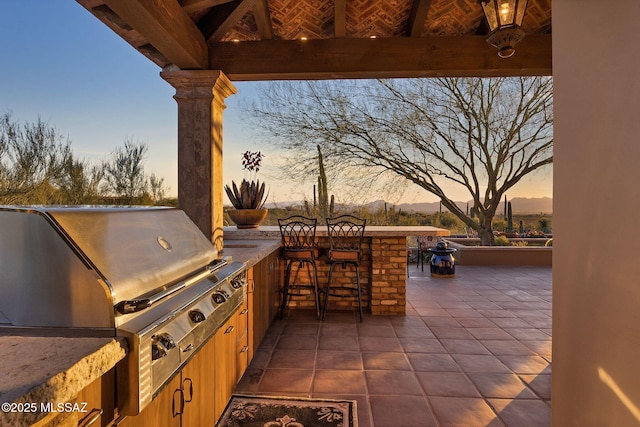 patio terrace at dusk featuring grilling area, an outdoor kitchen, and outdoor wet bar