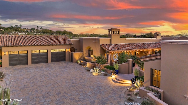 view of front of house featuring a garage, a tile roof, decorative driveway, and stucco siding