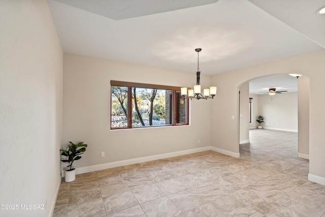 unfurnished room with arched walkways, ceiling fan with notable chandelier, and baseboards