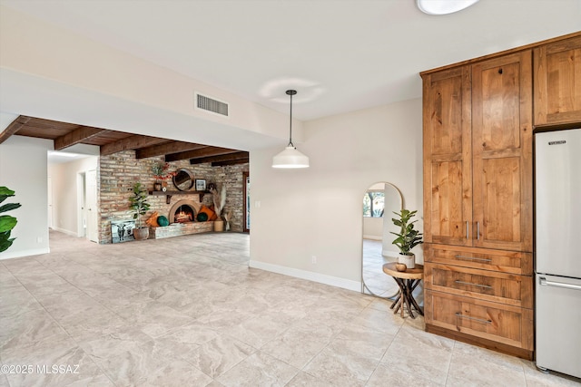 interior space with visible vents, freestanding refrigerator, a brick fireplace, beamed ceiling, and baseboards