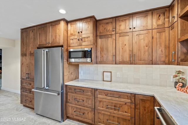 kitchen with stainless steel appliances, brown cabinets, light stone countertops, and decorative backsplash