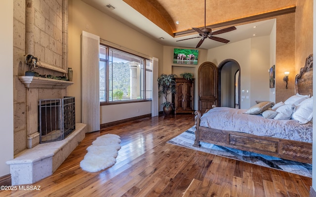 bedroom with visible vents, baseboards, a fireplace, wood-type flooring, and a raised ceiling