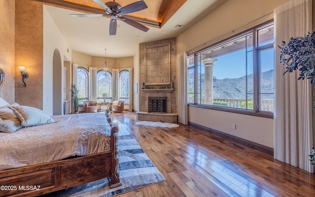 bedroom featuring a mountain view, wood-type flooring, arched walkways, a fireplace, and baseboards