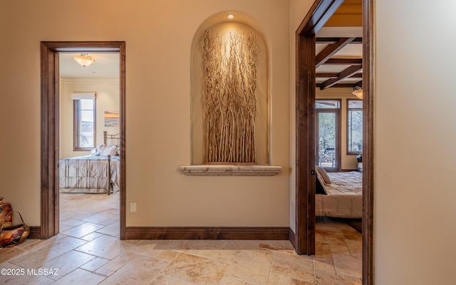 corridor with beamed ceiling, baseboards, and stone tile flooring