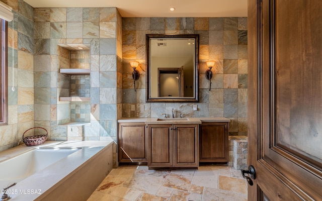 full bath with stone tile flooring, a bathing tub, tile walls, and vanity