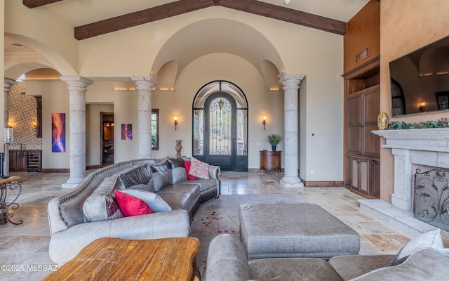 living room featuring decorative columns, baseboards, high vaulted ceiling, and stone tile floors