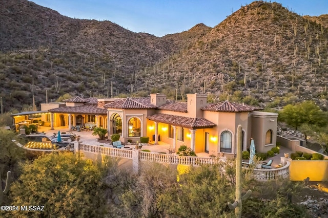 back of property featuring a tiled roof, stucco siding, a chimney, a patio area, and a mountain view