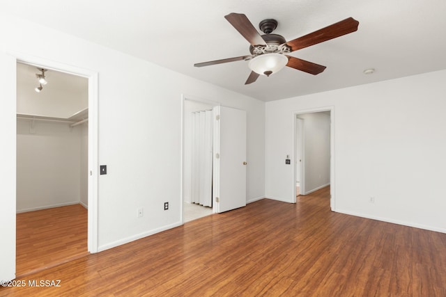 unfurnished bedroom with a ceiling fan, a spacious closet, baseboards, and wood finished floors