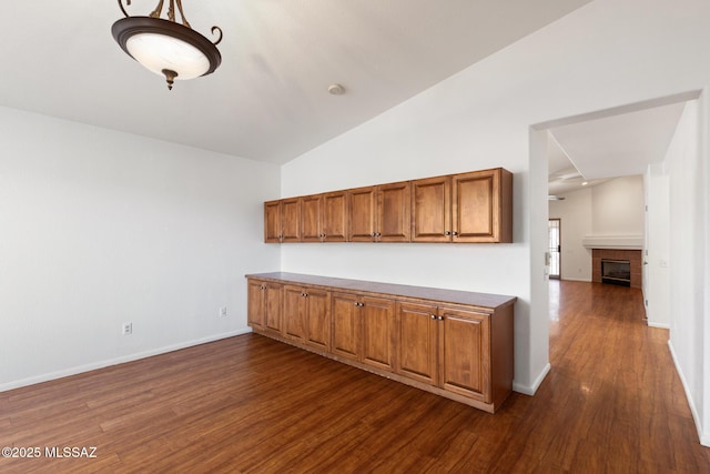 kitchen featuring baseboards, a tile fireplace, lofted ceiling, brown cabinets, and dark wood-style flooring