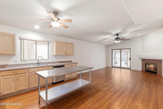 kitchen with dishwasher, a tiled fireplace, light wood-style floors, light brown cabinets, and a sink