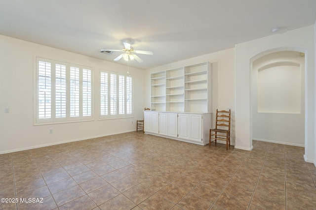 tiled empty room with ceiling fan, built in shelves, visible vents, and baseboards