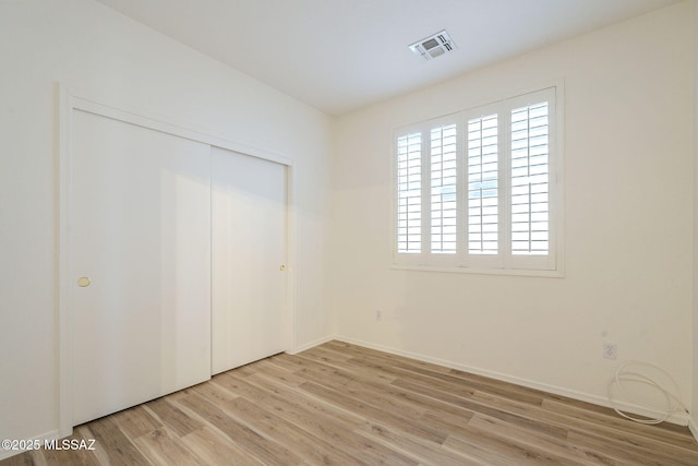 unfurnished bedroom with a closet, wood finished floors, visible vents, and baseboards