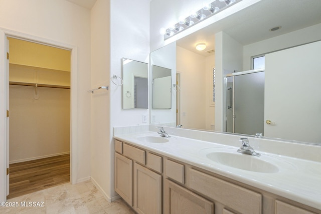 full bath with double vanity, a stall shower, a sink, and a walk in closet