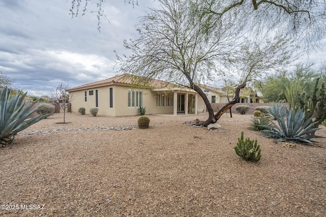 rear view of property featuring a patio, fence, a tile roof, and stucco siding