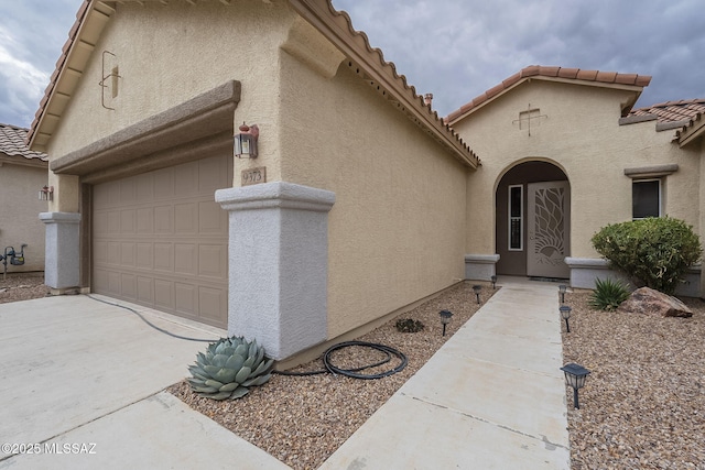 view of exterior entry with a tile roof, driveway, an attached garage, and stucco siding