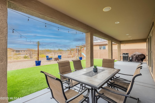 view of patio / terrace featuring grilling area, outdoor dining space, a playground, and a fenced backyard