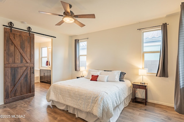 bedroom with a barn door, wood finished floors, baseboards, and ensuite bathroom