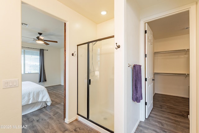 bathroom featuring a spacious closet, a stall shower, ceiling fan, and wood finished floors