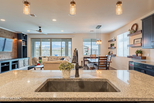 kitchen featuring ceiling fan, open floor plan, light stone counters, hanging light fixtures, and a sink