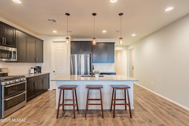 kitchen with light stone counters, wood finished floors, visible vents, a sink, and appliances with stainless steel finishes