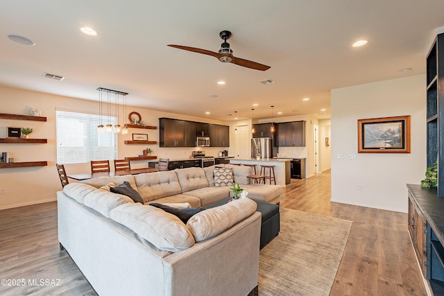 living area featuring light wood-type flooring, visible vents, recessed lighting, and ceiling fan with notable chandelier