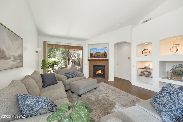 tiled living room with a tiled fireplace, built in features, visible vents, and vaulted ceiling