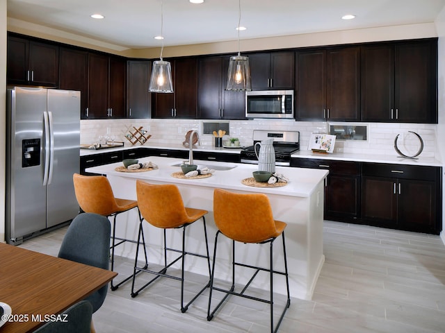 kitchen with light countertops, a kitchen breakfast bar, appliances with stainless steel finishes, and a sink