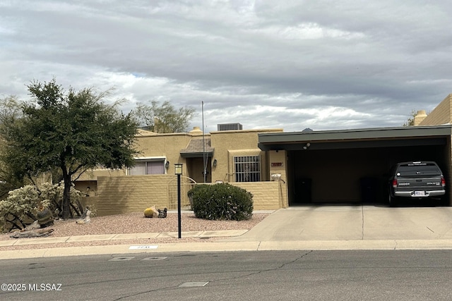 view of front of home featuring a carport, a fenced front yard, concrete driveway, and stucco siding