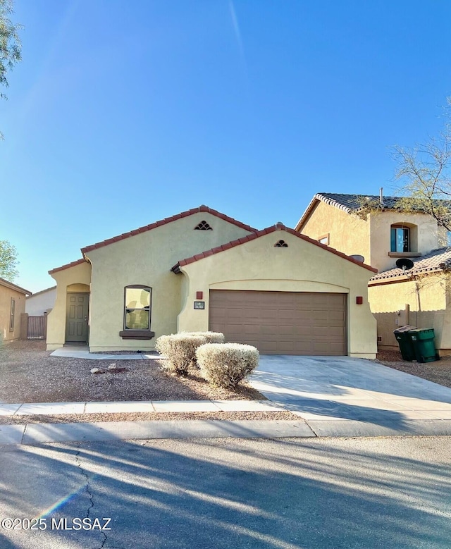 mediterranean / spanish house featuring driveway, an attached garage, a tiled roof, and stucco siding