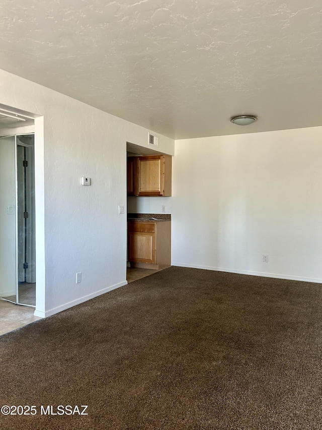 unfurnished living room featuring a textured ceiling, dark colored carpet, visible vents, and baseboards