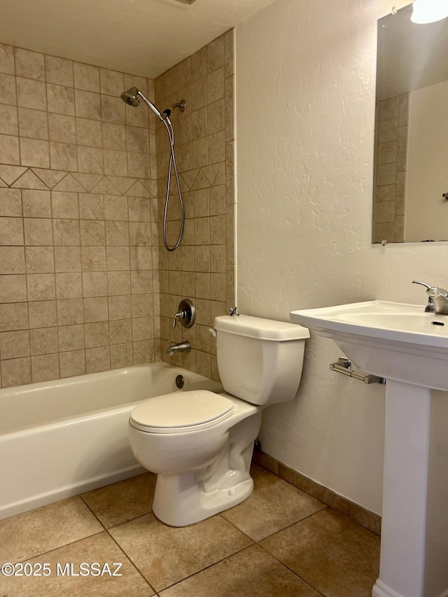 bathroom featuring baseboards, toilet, shower / bath combination, a textured wall, and tile patterned floors