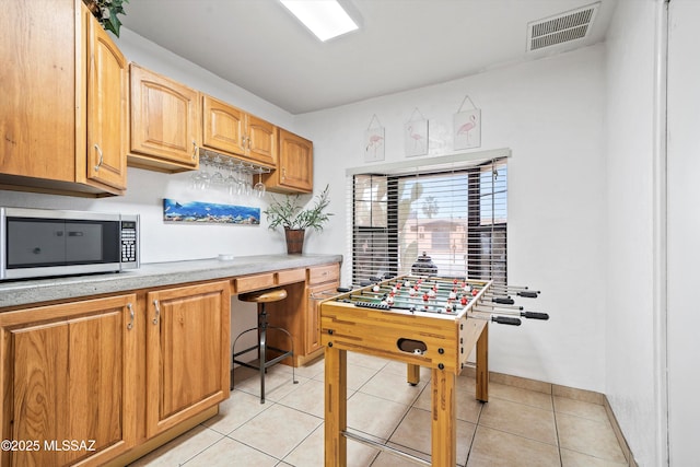 kitchen featuring light tile patterned floors, light countertops, stainless steel microwave, and visible vents